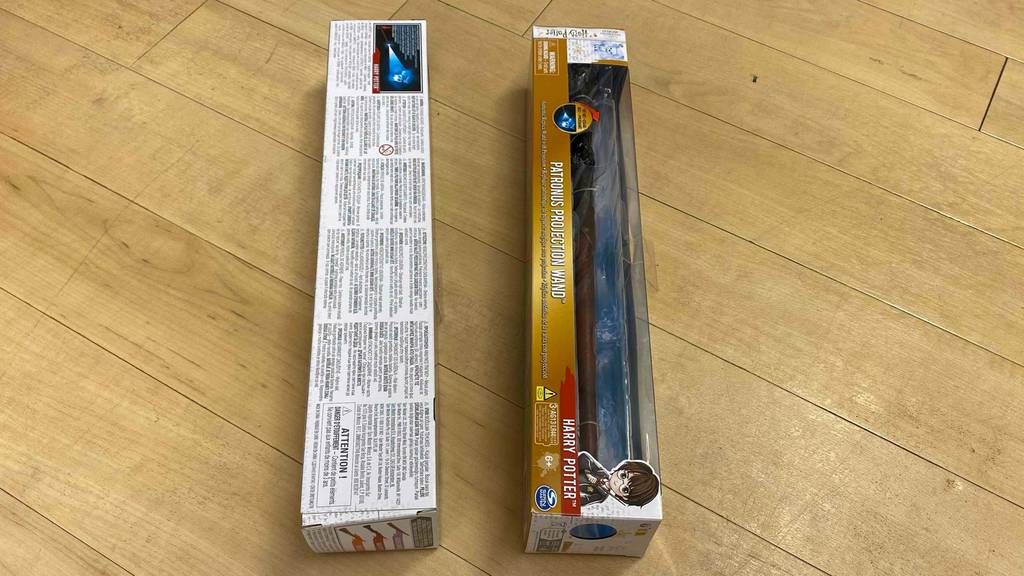 Im Test: Ein verpackter Harry Potter Zauberstab liegt neben einer weiteren Originalverpackung mit Rückseite nach oben auf einem Holzboden.