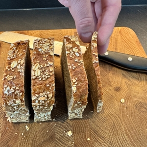 Eine Hand hält eine geschnittene Brotscheibe, die neben vielen weiteren Scheiben steht