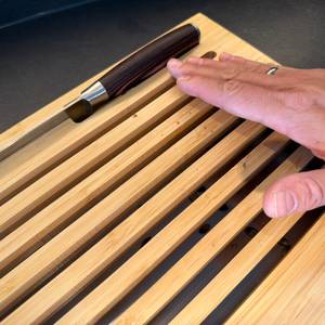 Krümel werden von einer Hand in die Ritzen vom WMF-Brotschneidebrett geschoben