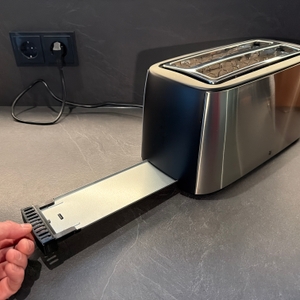 Eine Hand entfernt ein Blech für Krümel aus dem WMF-Bueno-Pro-Toaster
