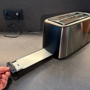 Eine Hand entfernt ein Blech für Krümel aus dem WMF-Bueno-Pro-Toaster