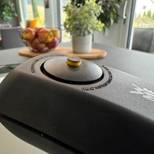Ein Knopf auf dem Deckel des WMF-Dampfkochtopfs ist nach unten gedrückt, nur der gelbe Pin ist zu sehen.