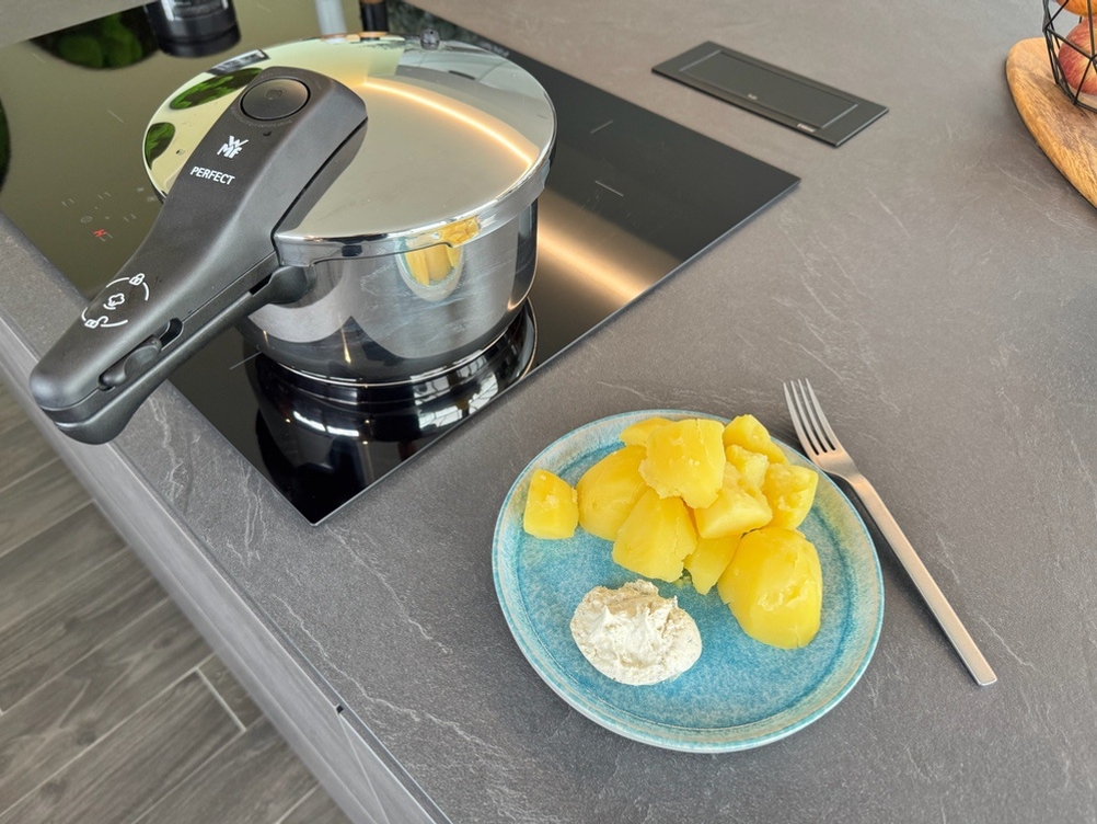 Ein Teller mit Kartoffeln und Kräuterquark und eine Gabel stehen neben dem WMF-Dampfkochtopf.