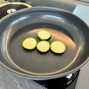 Vier Zucchinischeiben liegen noch nicht angebraten in einer Pfanne.