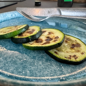 Vier Zucchinischeiben liegen angebraten auf einem blauen Teller