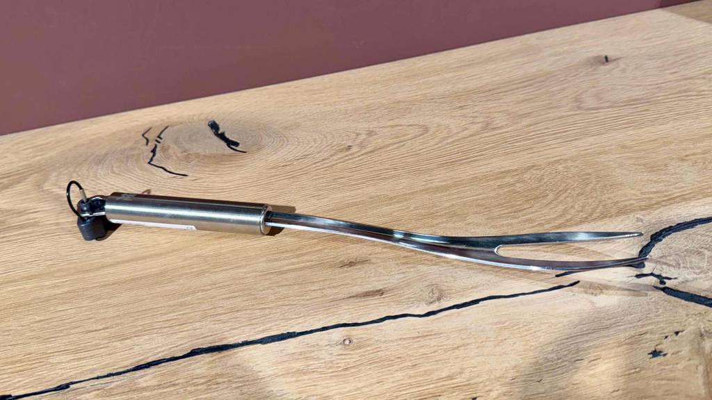 Eine getestete Edelstahl-Fleischgabel liegt auf einem Holzbrett.