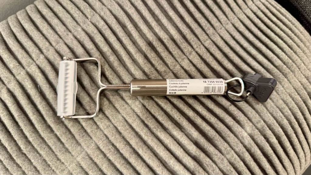 Ein getesteter Julienne-Schneider aus Edelstahl liegt auf einem hellen Kissen.