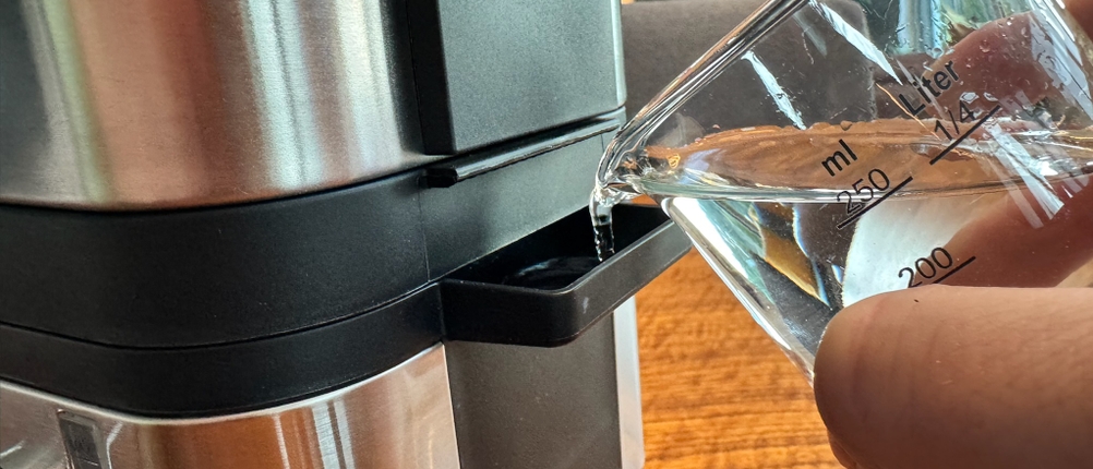 Eine Hand gießt mit Messbecher Wasser in den WMF KÜCHENminis Dampfgarer