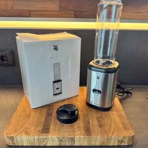 Der ausgepackte Smoothie-Maker von WMF steht neben der Originalverpackung auf einem Holzbrett.