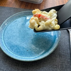 Mit einem Raclettespachtel werden mit Käse überbackene Nudeln in den vorderen Bereich der Pfanne geschoben. 