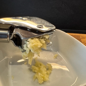 Nahaufnahme von gepresstem Knoblauch, der aus der Presse in eine Schale fällt.