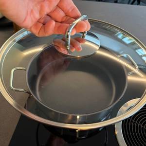 Eine Hand hält den Deckel der Wmf-Schmorpfanne 28 cm fest
