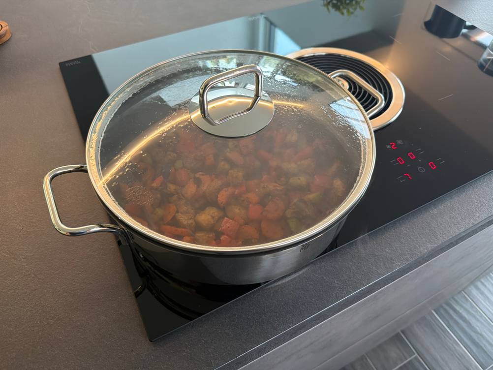 Die Wmf-Schmorpfanne 28 cm steht während des Kochens mit Deckel auf einer Kochplatte