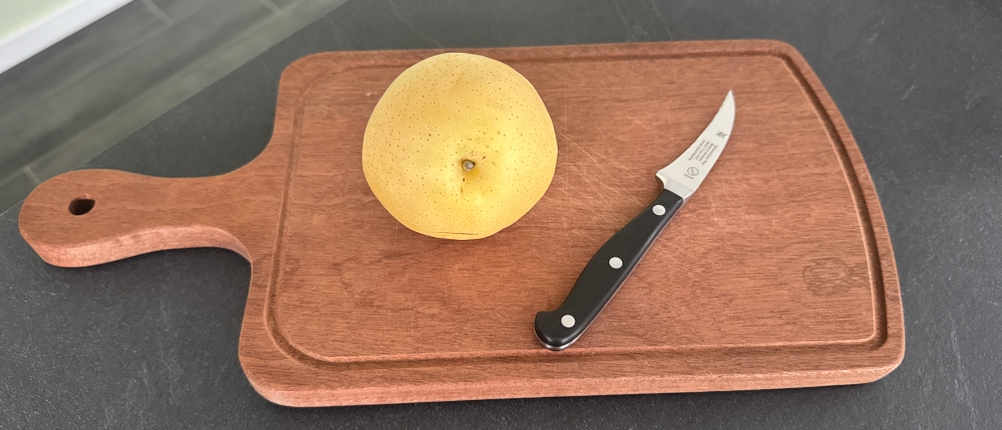 Das WMF Spitzenklasse Plus liegt neben einer Nashi-Birne auf einem Arbeitsbrett.