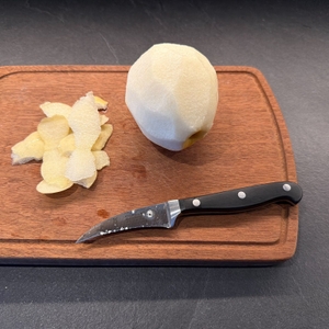 Das WMF-Schälmesser liegt neben einer geschälten Nashi-Birne auf einem Brett.