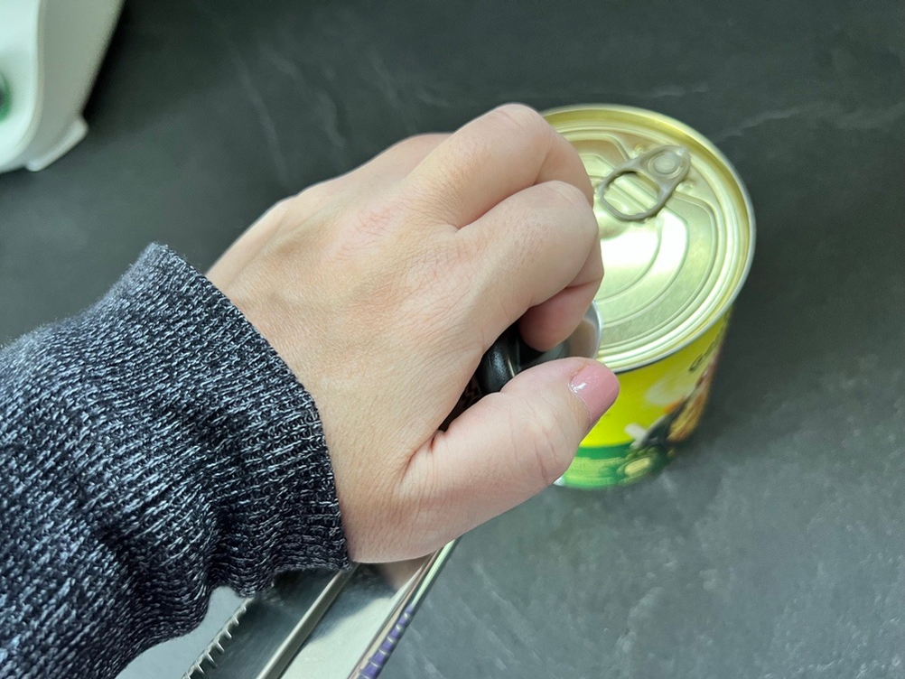 Eine Hand greift den Dosenöffner WMF-Tin-Up, der auf einer Dose liegt.