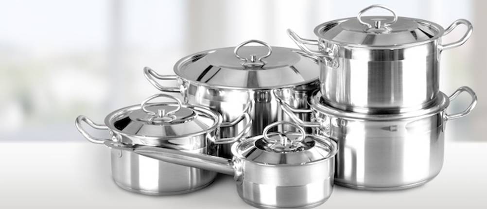 Das Design von WMF-Topfsets getestet: Ein fünfteiliges Edelstahl-Topfset mit vier Kochtöpfen und einem Stieltopf steht auf einer Ablage vor einem weißen Hintergrund. Alle Töpfe haben Edelstahldeckel.