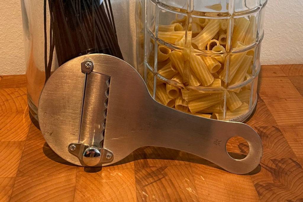 Trüffelhobel im Test: Ein Trüffelhobel lehnt an einem Glas mit schwarzen Spaghetti und einem Glas Nudeln.