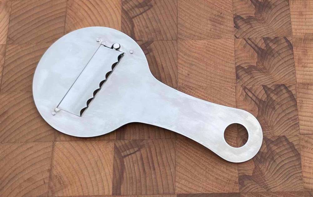 Trüffelhobel im Test: Ein Trüffelhobel liegt schräg auf einem Holzbrett.