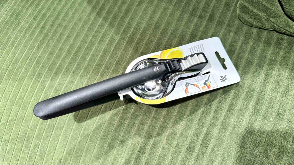 Test: Eine Edelstahl-Zitronenpresse mit schwarzem Griff liegt auf einem grünen Gewebe.