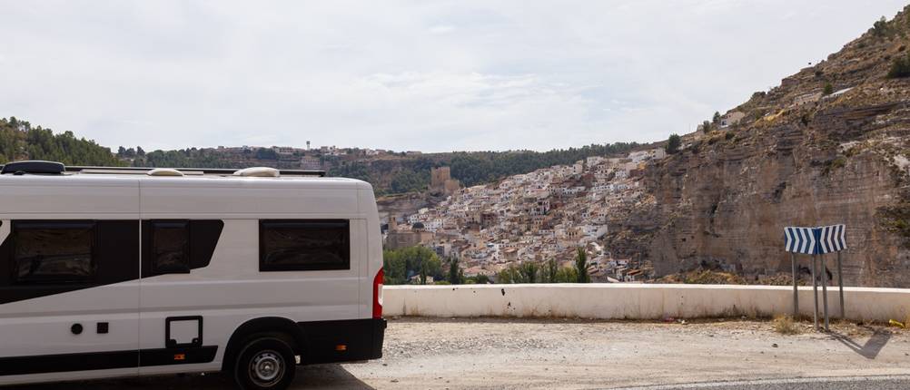 Weißes Wohnmobil parkt auf einer Küstenstraße mit Blick auf ein spanisches Bergdorf
