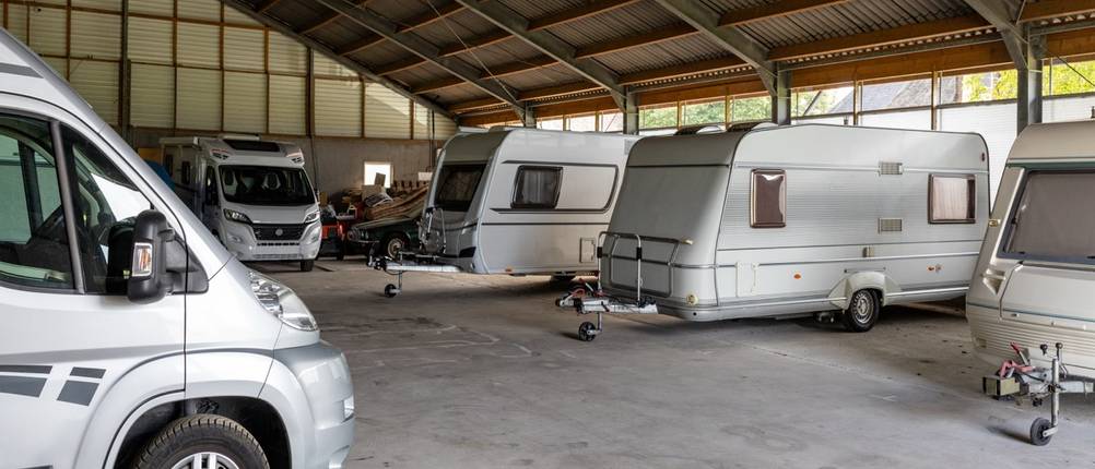 Mehrere Wohnwagen und Wohnmobile stehen eingelagert in einer großen Scheune auf einem Bauernhof