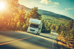 Wohnmobilversicherung im Test: Weißes Wohnmobil fährt eine Straße entlang.