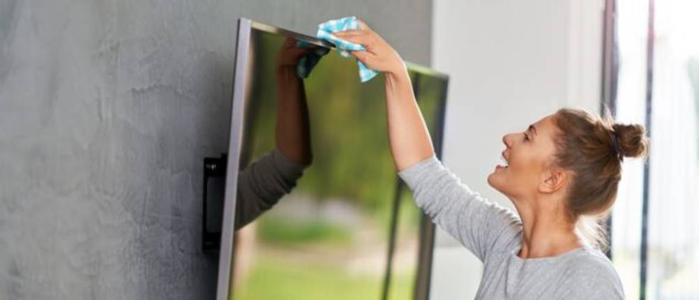 Frau reinigt einen Fernseher mit einem Lappen.
