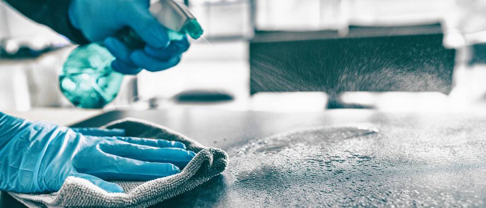 Tisch wird mit einer Sprühflasche, Handschuhen und Putzlappen gereinigt.