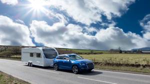 Wohnwagenversicherungen im Test: Bei sonnigem Wetter fährt ein blauer Wagen mit einem Wohnwagen auf einer Straße.