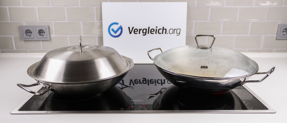 Zwei Woks mit Deckel stehen nebeneinander auf einem Kochfeld.