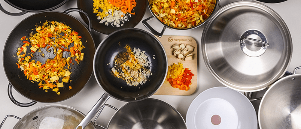 Ansicht von oben auf verschiedene Woks mit und ohne Deckel sowie Gemüse