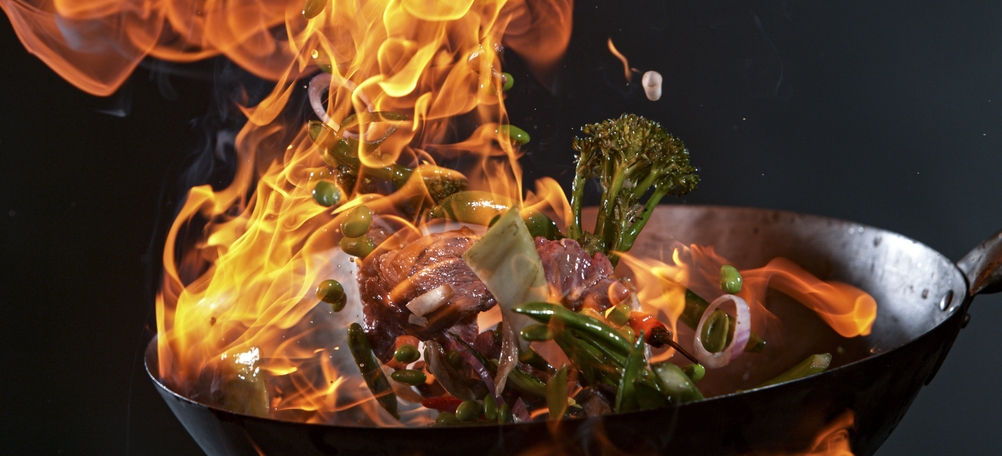 Wokpfannen im Test: Wokpfanne mit angebratenem Gemüse, die unter Flammenbildung geschwenkt wird