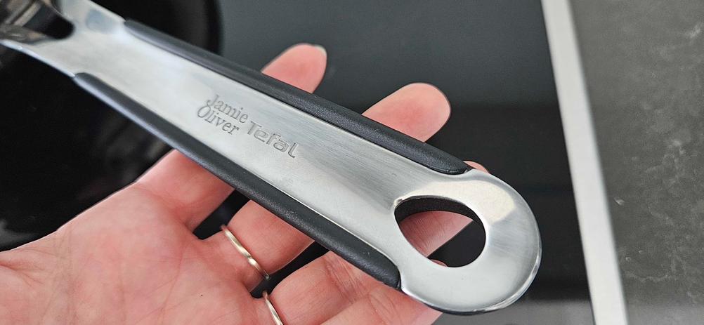 Wokpfannen im Test: Nahaufnahme einer Hand, die den Stiel der getesteten Wokpfanne mit Logo hält.