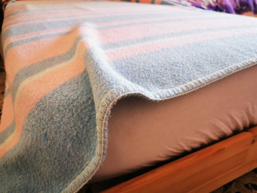 Detailansicht des Materials einer auf einem Bett liegenden Wolldecke im Test.