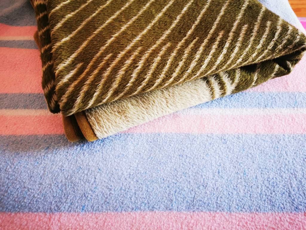 Eine zusammengelegte Wolldecke in grün-weißem Muster liegt getestet auf einer hellen rosa-blauen.