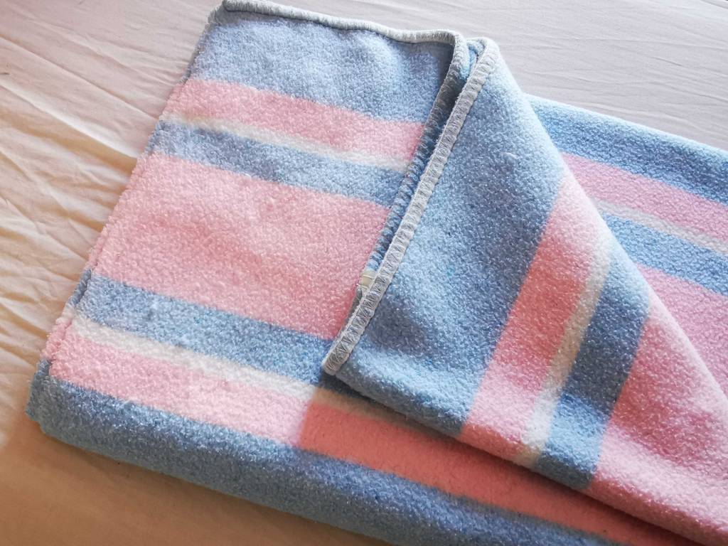 Im Test: Eine rosa-blaue Wolldecke liegt halb aufgeschlagen auf einem Bett.