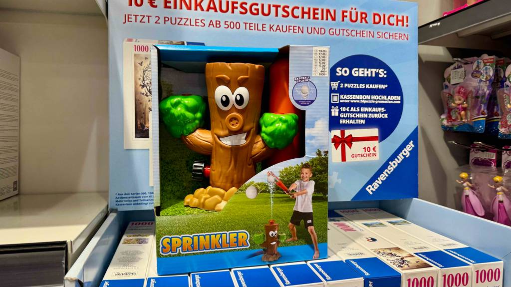 Eine Verpackung mit dem getesteten Wassersprinkler für Kinder im Baumstamm-Design steht auf mehreren Packungen mit Puzzles.