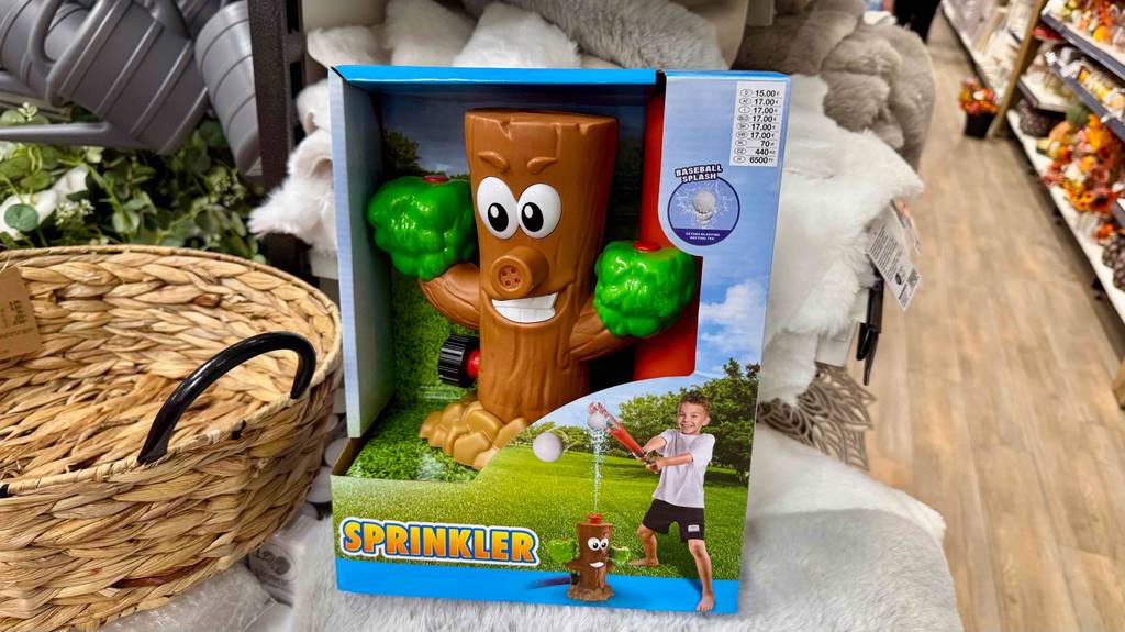 Der getestete Wassersprinkler für Kinder im Baumstamm-Design in einer Packung mit Preisetikett steht auf einem Verkaufsregal.