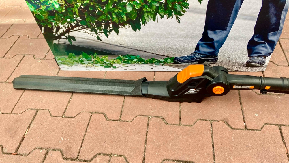 Im Test: Nahaufnahme des Motors und der geschützten Schneideblätter vor einem Plakat auf einem Pflasterboden.