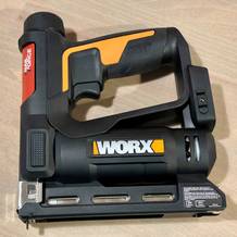 Ausgepackter WORX WX843.9 Akku-Tacker mit Anleitung, Klammern und Originalverpackung auf einem Holztisch. Der Lieferumfang liegt vollständig bereit zur Inbetriebnahme.