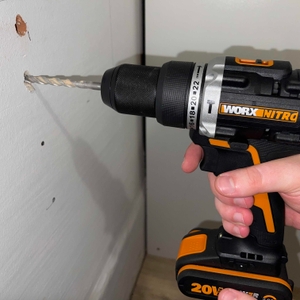 Der Worx Nitro WX352 Akkubohrer bohrt ein Loch in eine weiße Wand. Die Hand des Nutzers führt das Werkzeug stabil.
