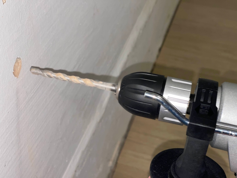 Die Worx-WX318-Schlagbohrmaschine beim Bohren in eine weiße Wand. Der Bohrer dringt kontrolliert in den Untergrund ein, während sich Bohrstaub am Ansatzpunkt bildet.