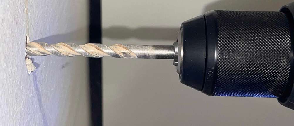 Makroaufnahme eines Bohrvorgangs mit dem Worx Nitro WX352 in eine weiße Wand. Die Bohrspitze ist kurz vor dem vollständigen Eindringen.