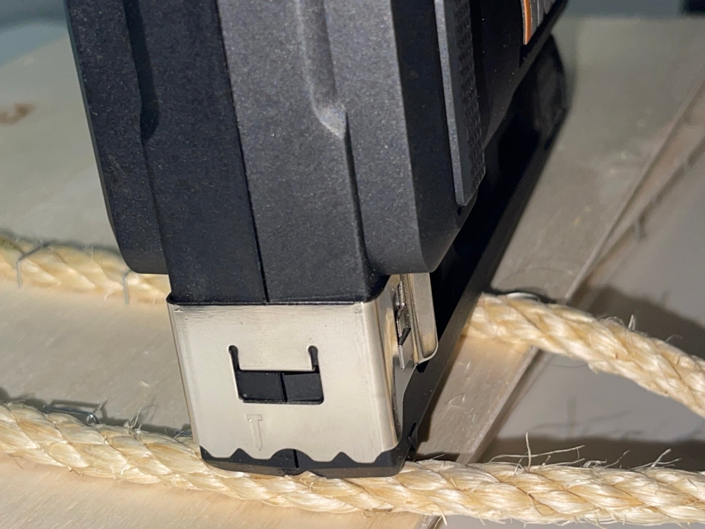 Nahaufnahme des WORX WX843.9 Akku-Tackers beim Tackern eines Seils auf eine Holzplatte.