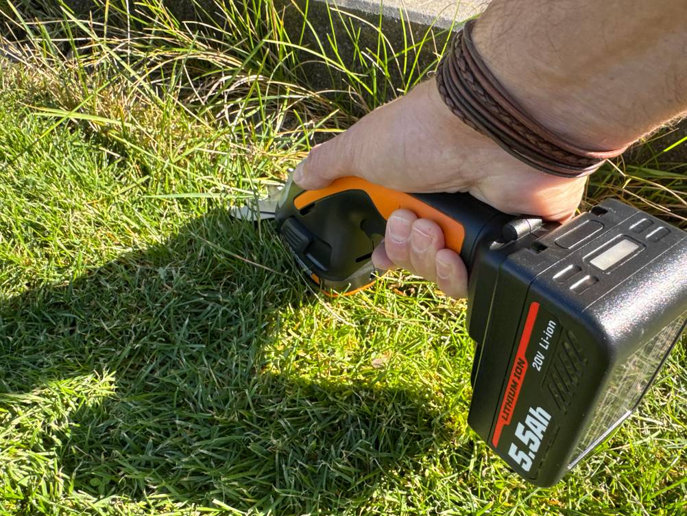 Eine Hand schneidet mit der Worx WG801E.9 kurzes Gras.