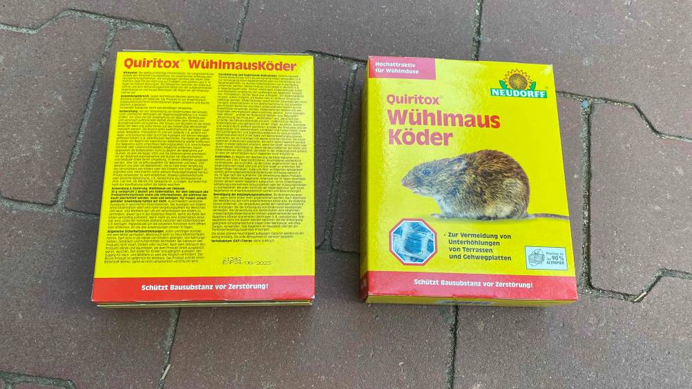 Auf dem Boden liegen sich zwei getestete Wühlmausköder für Gehwege und Terrassen. 
