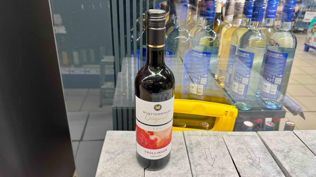Trollinger im Test: Die Flasche Wein steht auf mehreren Kartons neben einem Weinregal im Supermarkt.