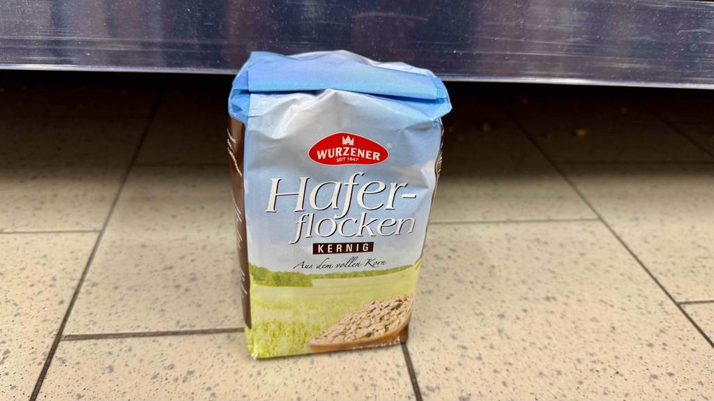 Eine 500-g-Packung mit kernigen Haferflocken im Test steht auf dem Boden vor einem Regal.