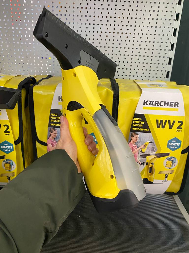 Hand hält einen gelben getesteten Kärcher-Fenstersauger vor seiner Originalverpackung, die auf einem Verkaufsregal steht.